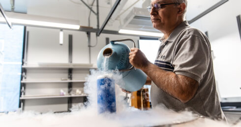Pinder pours liquid nitrogen into a blue cannister to prepare for the superconductor levitation track demonstration at UBC.